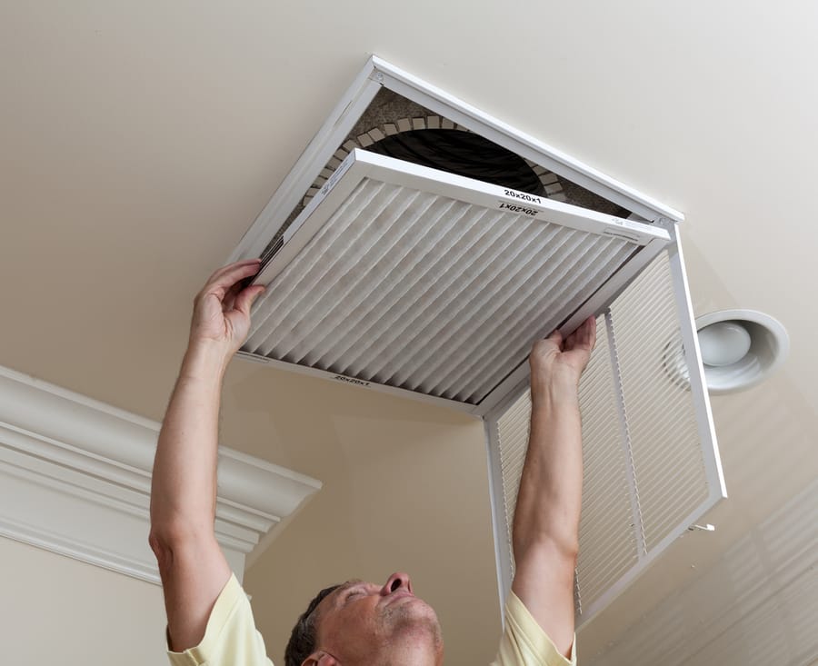 HVAC tech opening air conditioning filter in ceiling.
