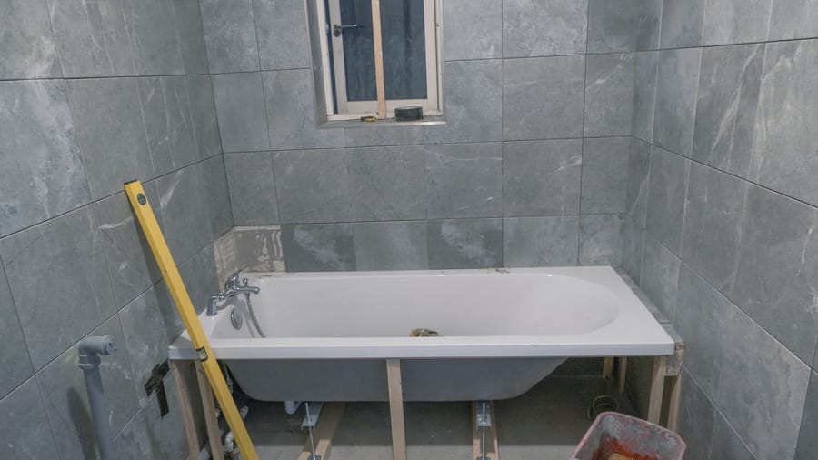 A bathtub being installed in bathroom.